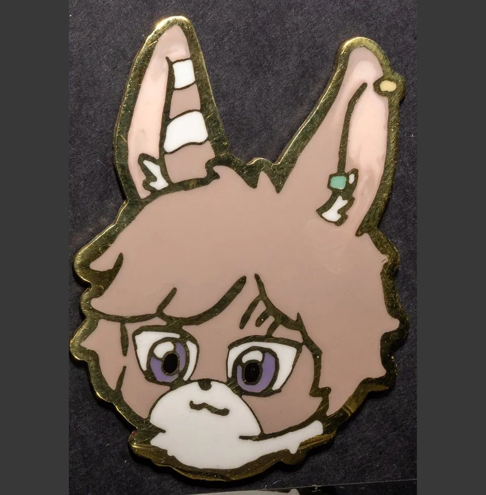 Enamel pin of a brown bunny with long ears, an ear piercing and purple eyes.